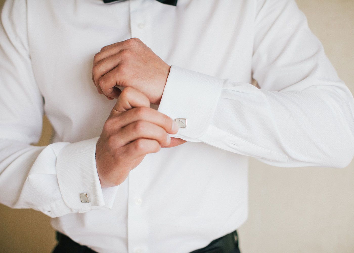 Close up of a groom in a white dress shirt putting on cufflinks.