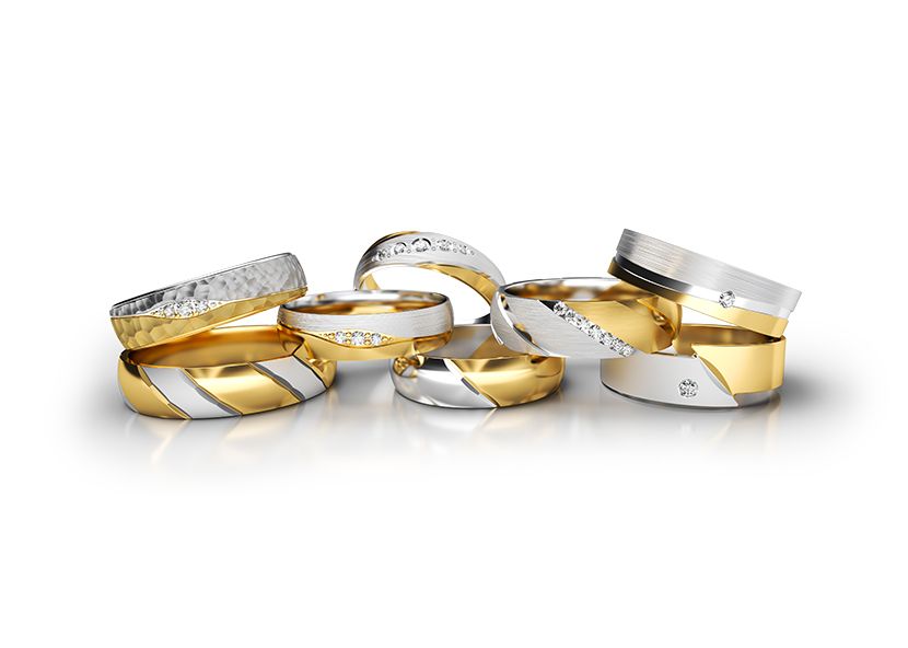 A stack of two-toned diamond rings of various desgins scattered on a white background